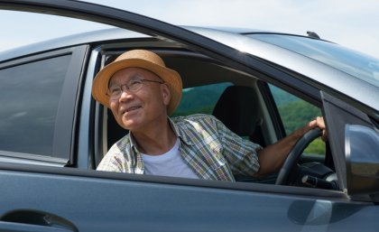 A man wearing a hat looks out the open door of a car.